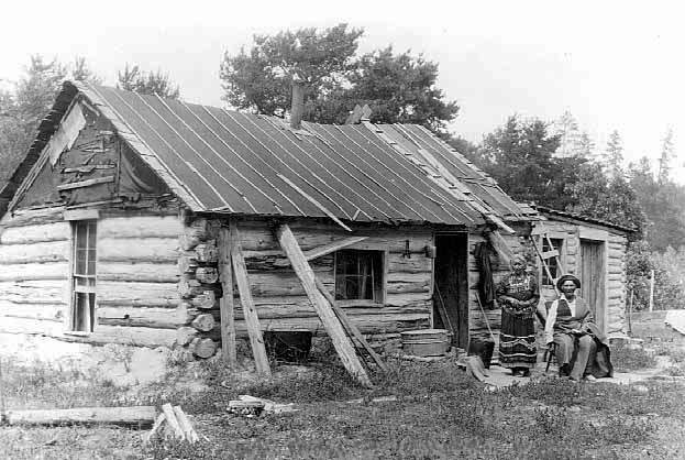 Indian man and woman by their log home, Deer River, 1930-1939.