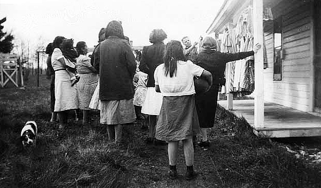Elmer Brunet, Indian agent, showing clothing to women and children, Mille Lacs, n.d.