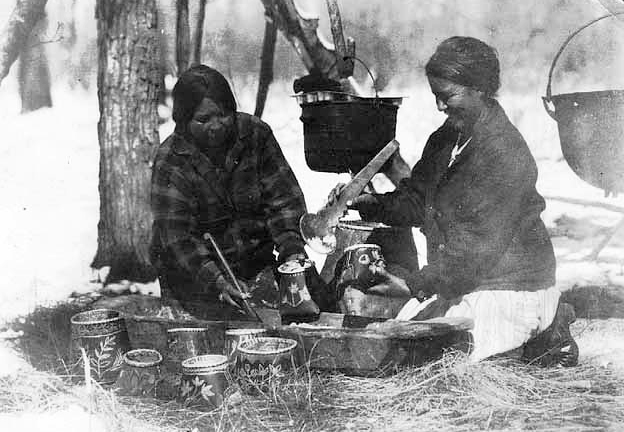 Mary Bigwind and Maggie Skinaway filling small baskets with maple sugar for sale in the store, Mille Lacs, ca. 1925.