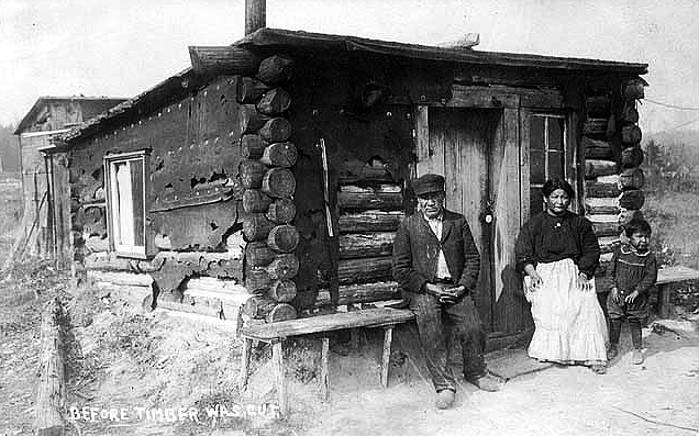 Indian family seated in front of log home, ca. 1910.