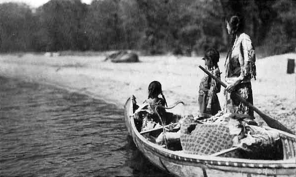 Ojibway Indian woman and two girls with loaded canoe heading for blueberry camp, 1920.