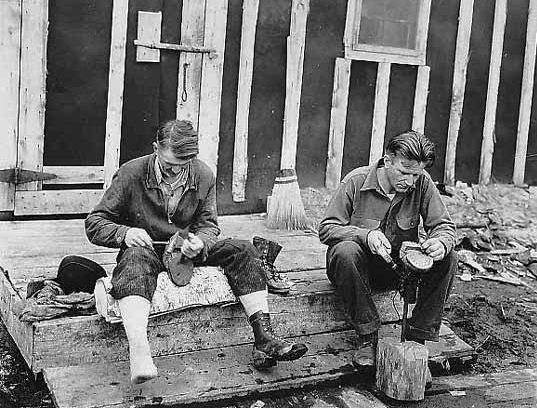 Two lumberjacks spending part of their Sunday repairing their shoes, ca. 1935.