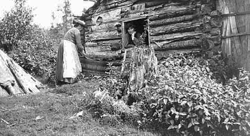 Mrs. Shingibis outside her cabin; Mrs. William Howenstine in window, Chippewa City, Grand Portage Reservation, 1905.