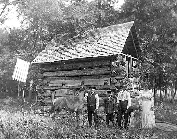 Family and horse posed by log barn, ca. 1900.