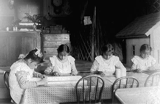 Young girls studying at a table at an Indian boarding school, location unknown, ca. 1900.