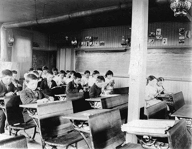 Children studying in a classroom at an Indian boarding school, location unknown, ca. 1900.