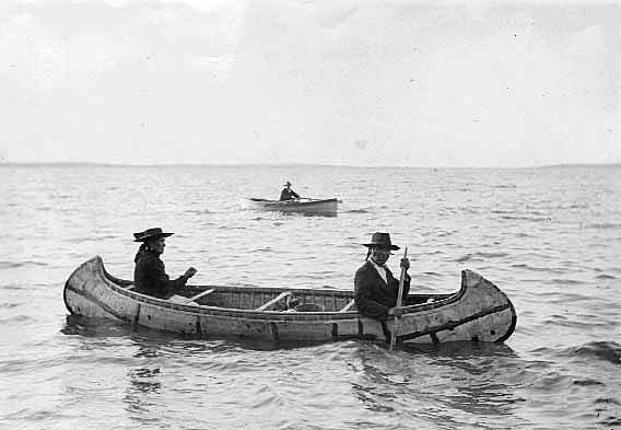 Ojibwe birch bark canoe [with wooden boat in the background], ca. 1910.