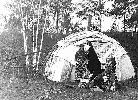 Tom Smith with woman and child in front of birch bark dwelling at Norway Beach, ca. 1920.