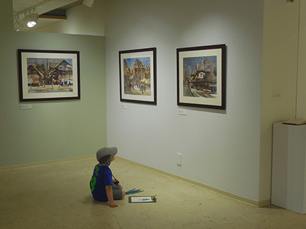 Child looking at art exhibit in Tweed Museum while sitting on floor.
